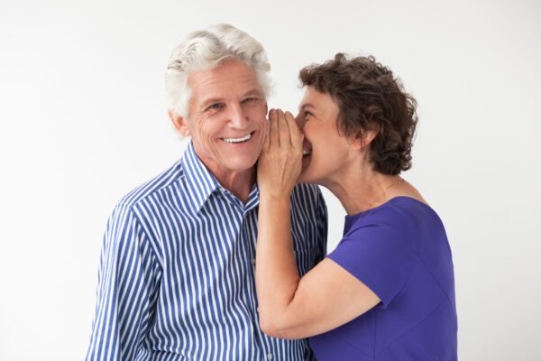 Closeup portrait of elderly woman whispering secret to her smiling husband. Isolated view on white background.